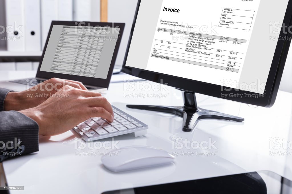 Close-up Of A Businessperson's Hand Checking Invoice On Computer At Workplace